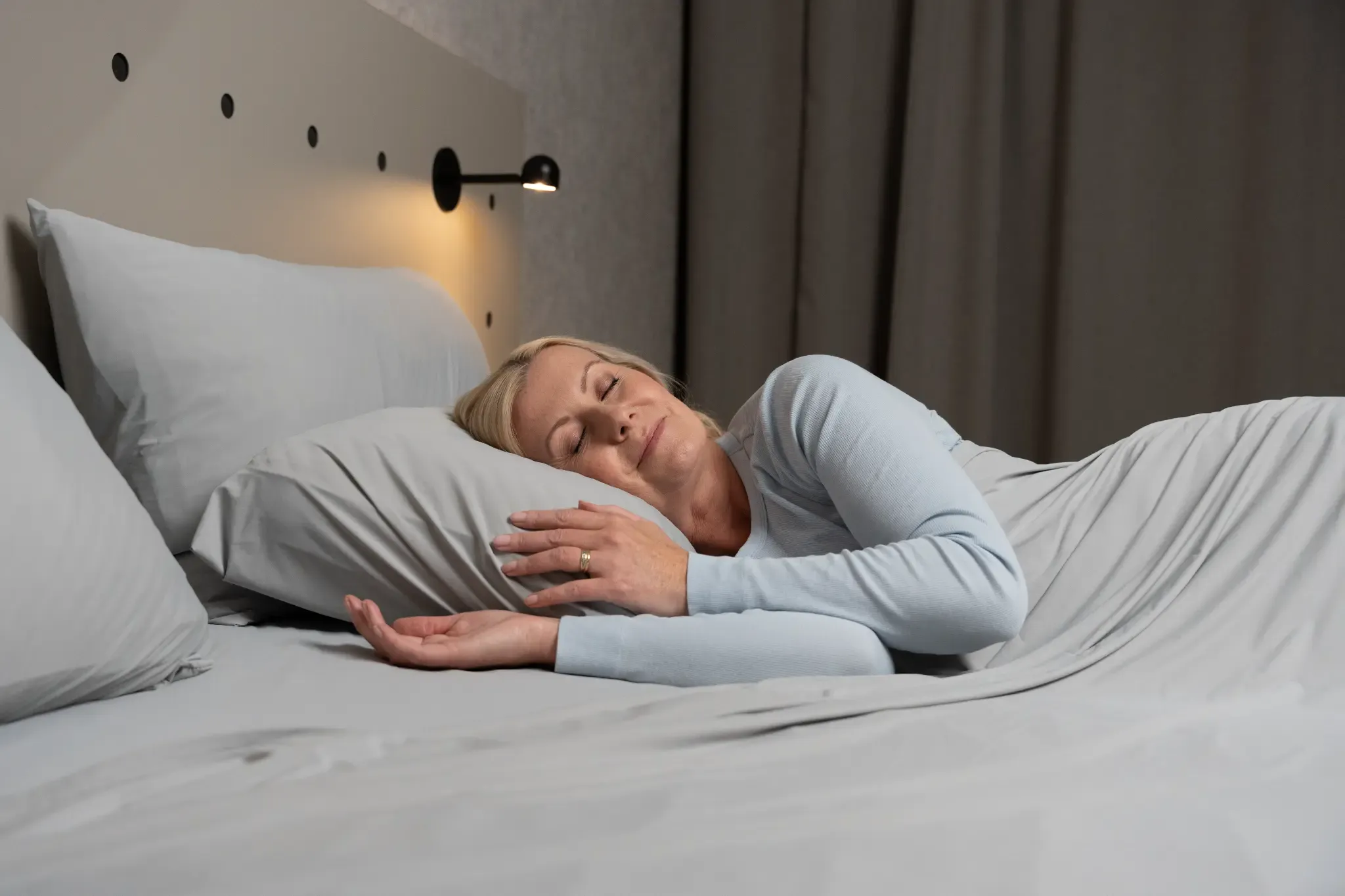 Woman sleeping peacefully in cool grey sheets under a soft bedside light