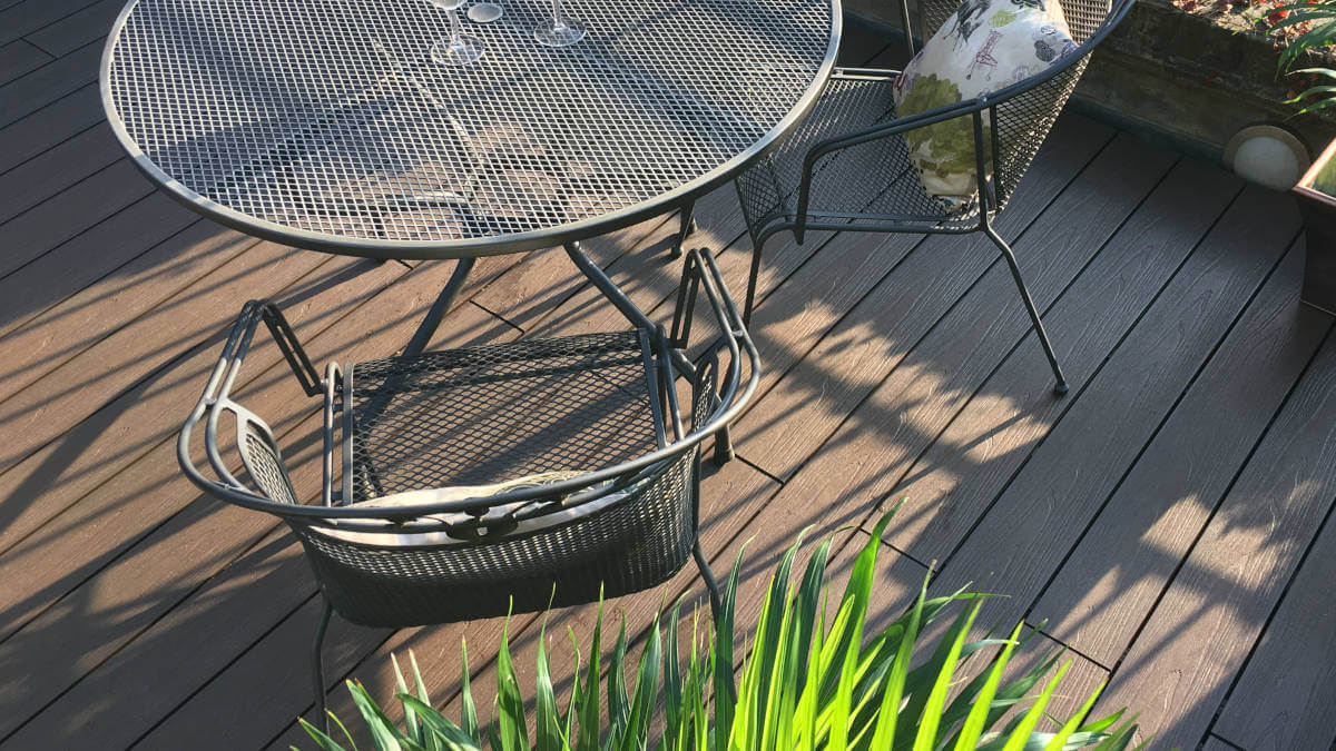 Metal table with two chairs and a bench on a wooden deck with plants nearby