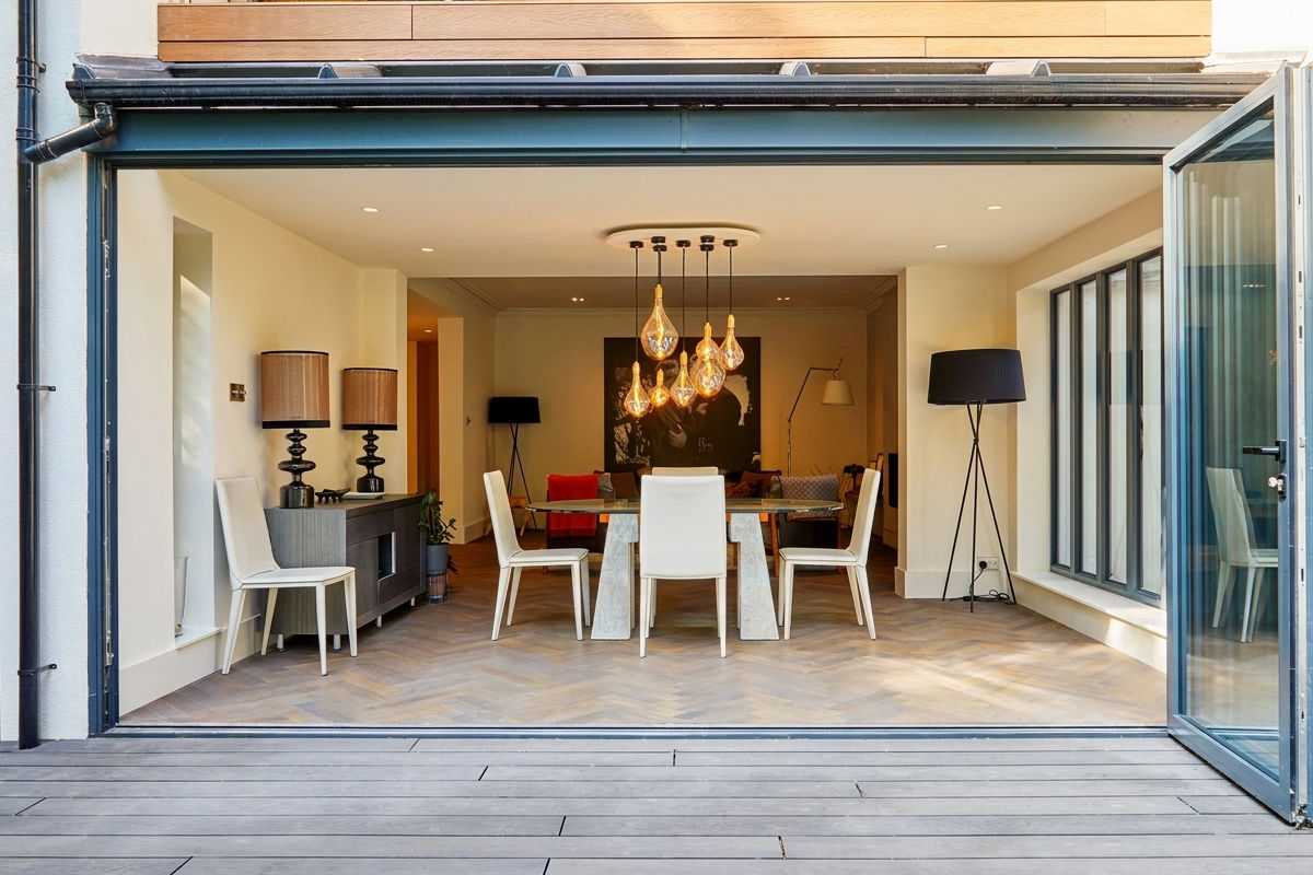 Dining area with white chairs, hanging lights, lamps, and open glass doors to outside