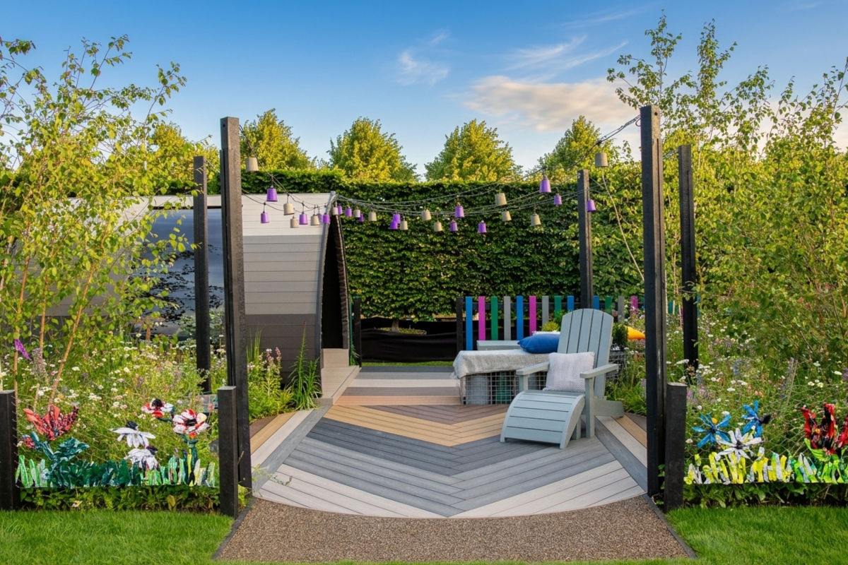Outdoor garden patio with lounge chairs, string lights, greenery, and decorative flowers