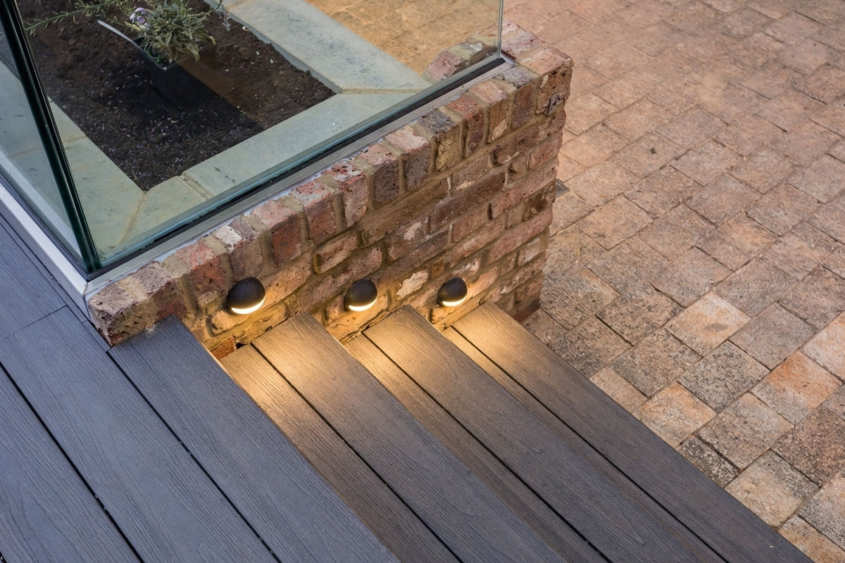 Wooden stairs with three round lights embedded in brick wall and a paved ground