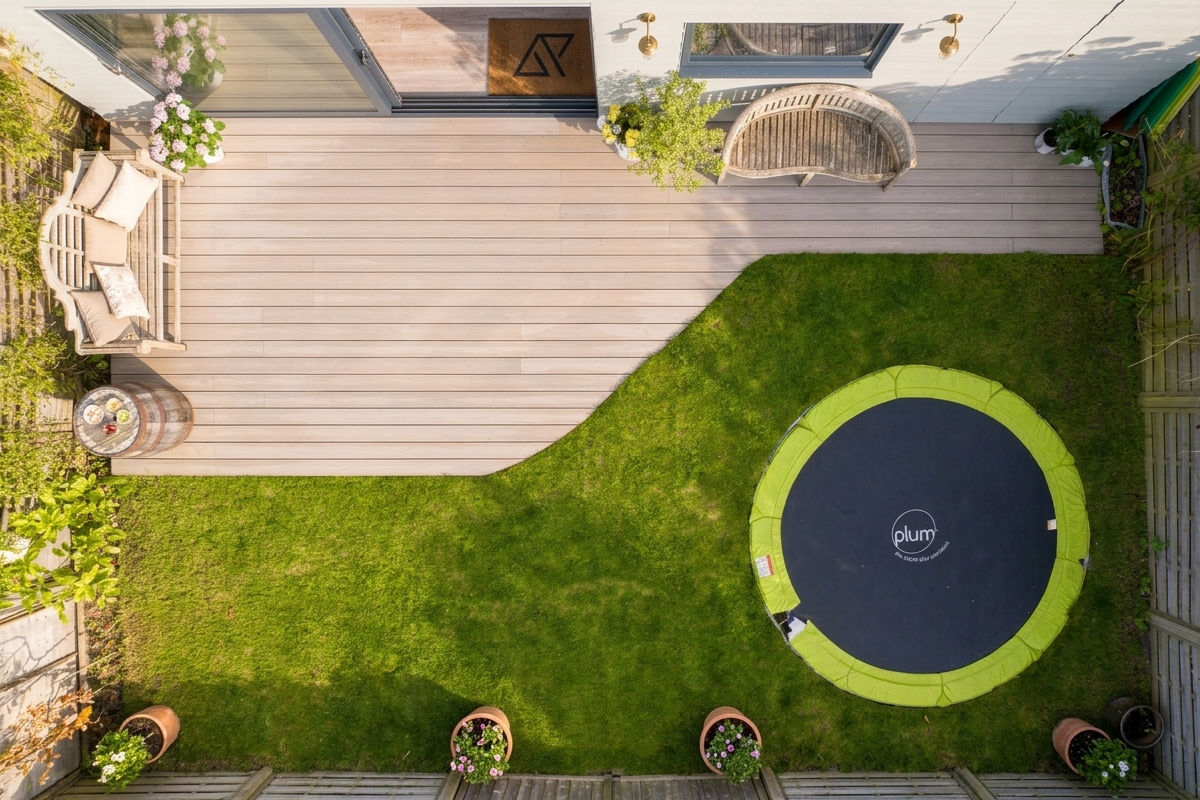 Top-down view of a backyard with a wooden deck, seating area, and round trampoline on grass