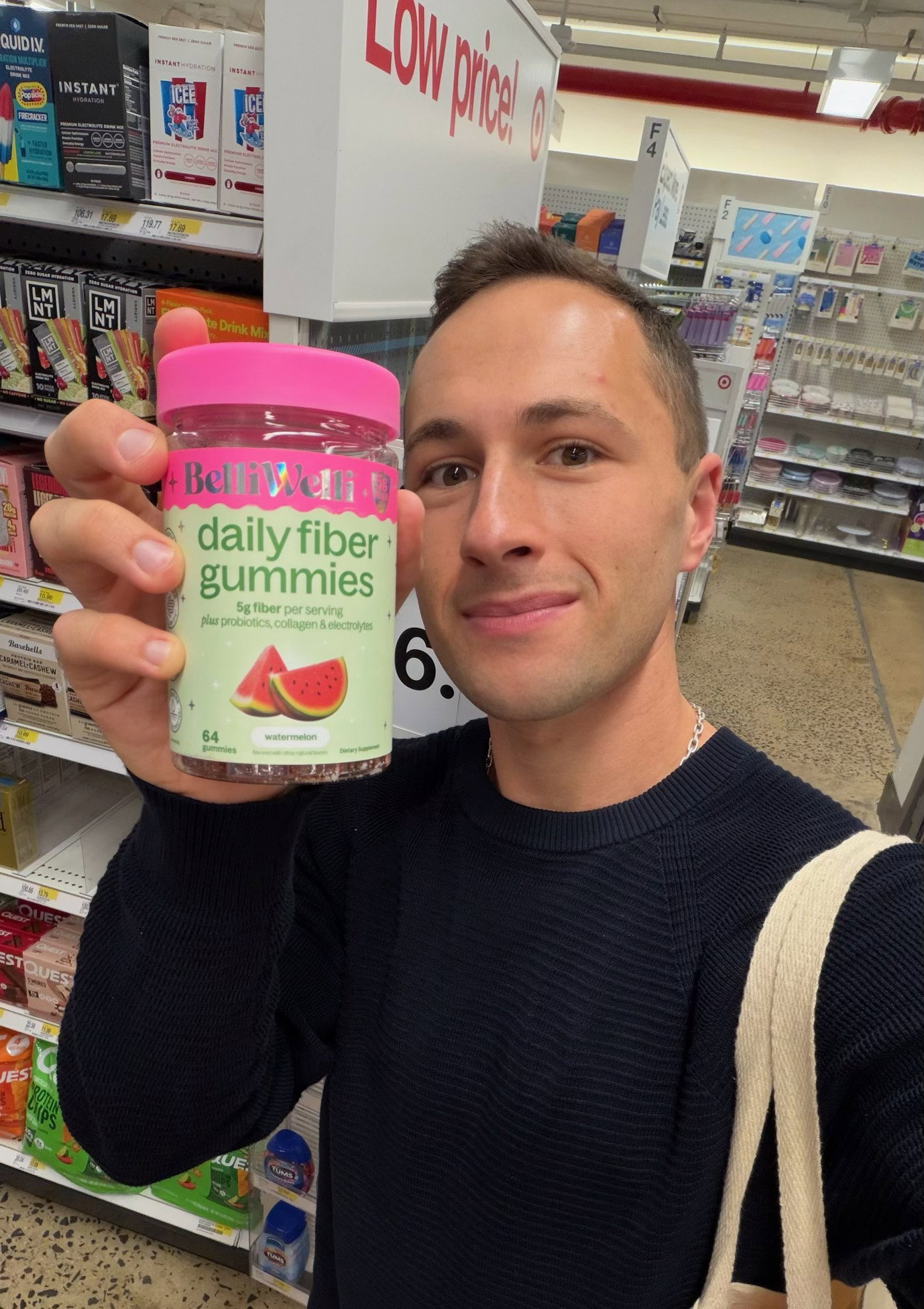 Smiling man in a navy sweater holding up a jar of BelliWelli Watermelon daily fiber gummies in a store aisle