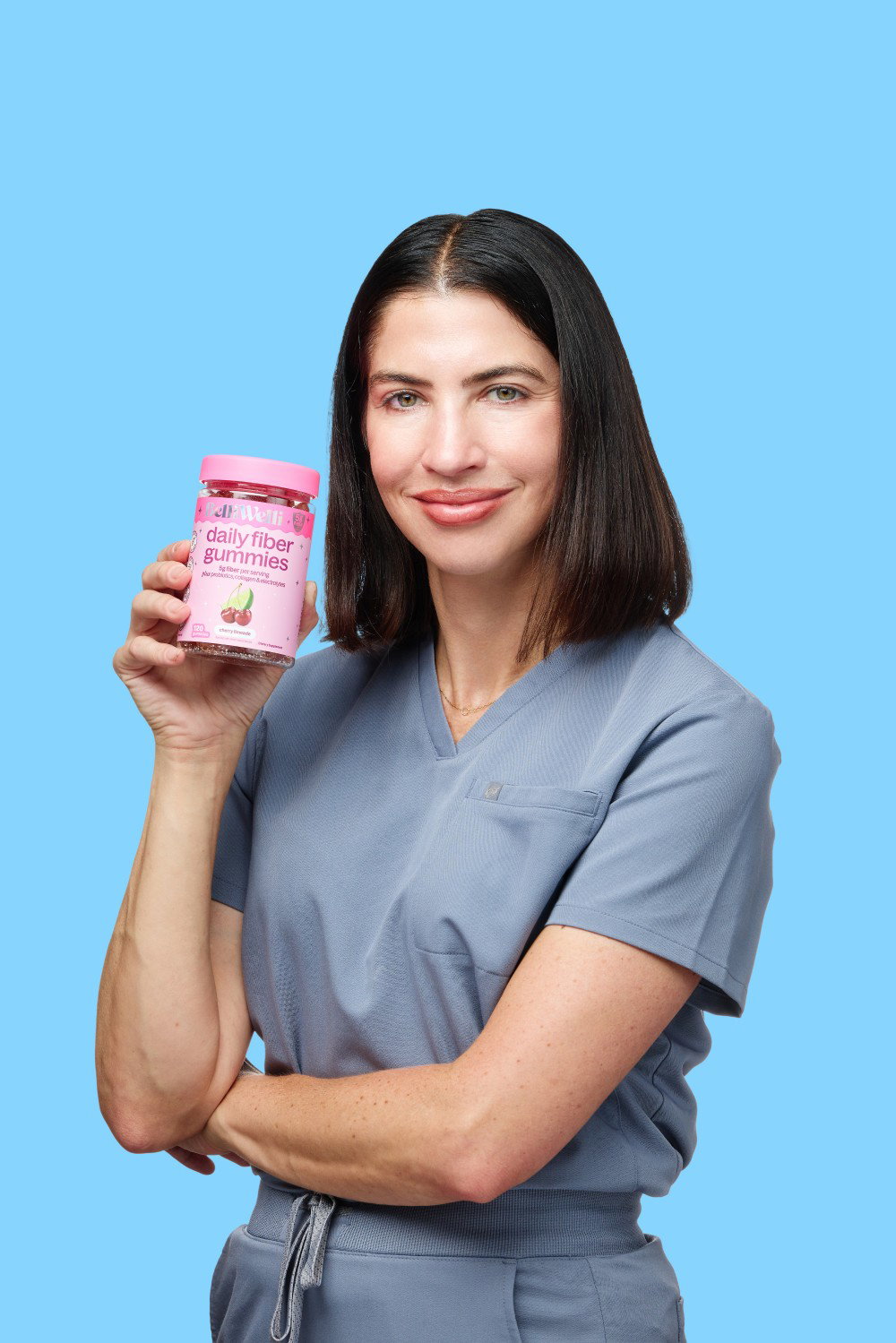 Dr. Jennah Siwak in blue scrubs smiling and holding up a jar of BelliWelli Cherry Limeade daily fiber gummies