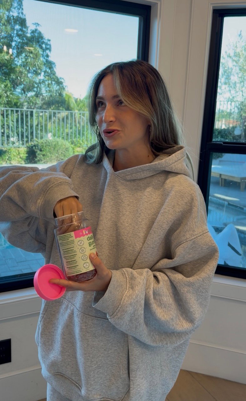 Woman in a grey hoodie reaching into an open jar of BelliWelli daily fiber gummies
