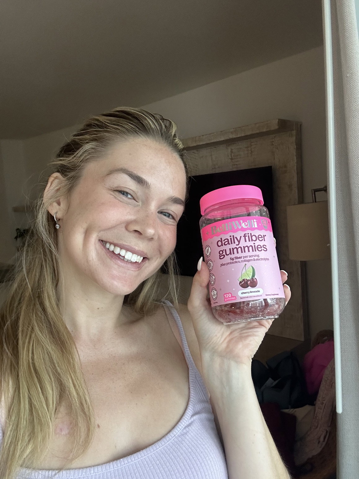 Smiling woman holding up a jar of BelliWelli cherry limeade daily fiber gummies