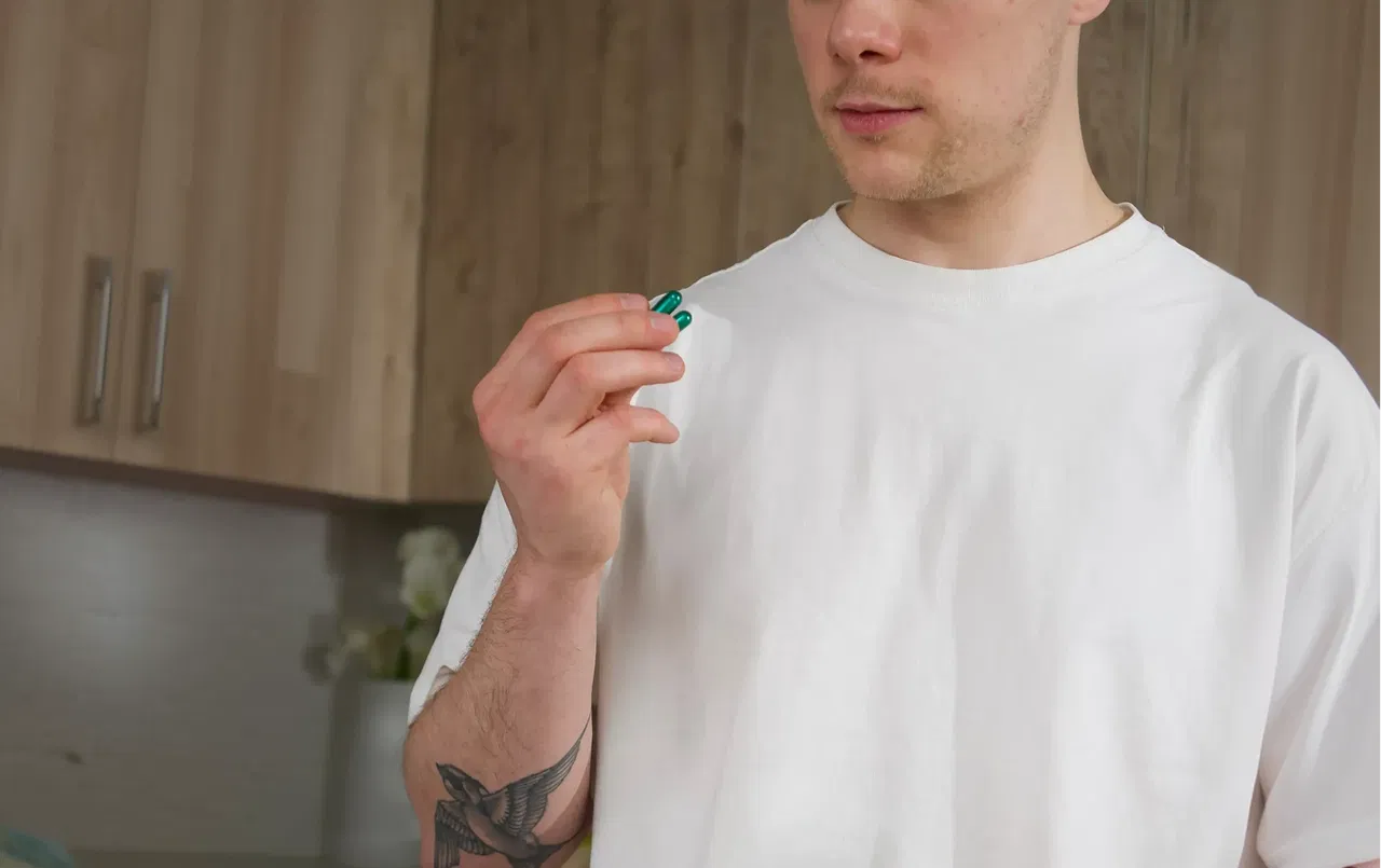 Чоловік тримає дві зелені капсули NS44 Focus Memory (Nooside44) у руці на фоні кухні, лайфстайл фото