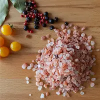 Rosa Salz, gelbe Tomaten, Pfefferkörner und Lorbeerblätter auf eine Holzunterlage stapeln.