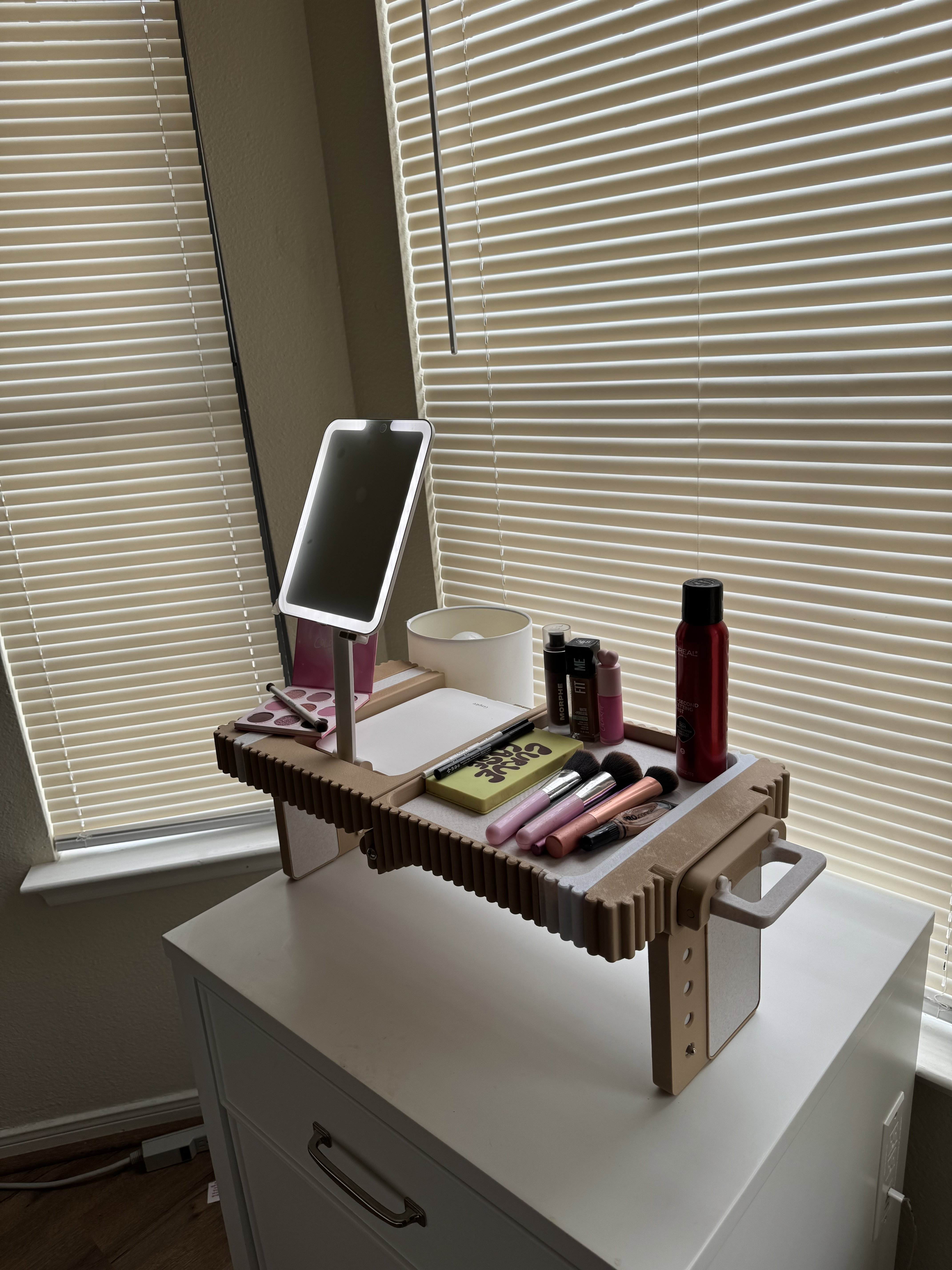 The Lap Vanity set up on a dresser by a sunlit window, LED mirror lit and trays filled with brushes, lip products and hairspray