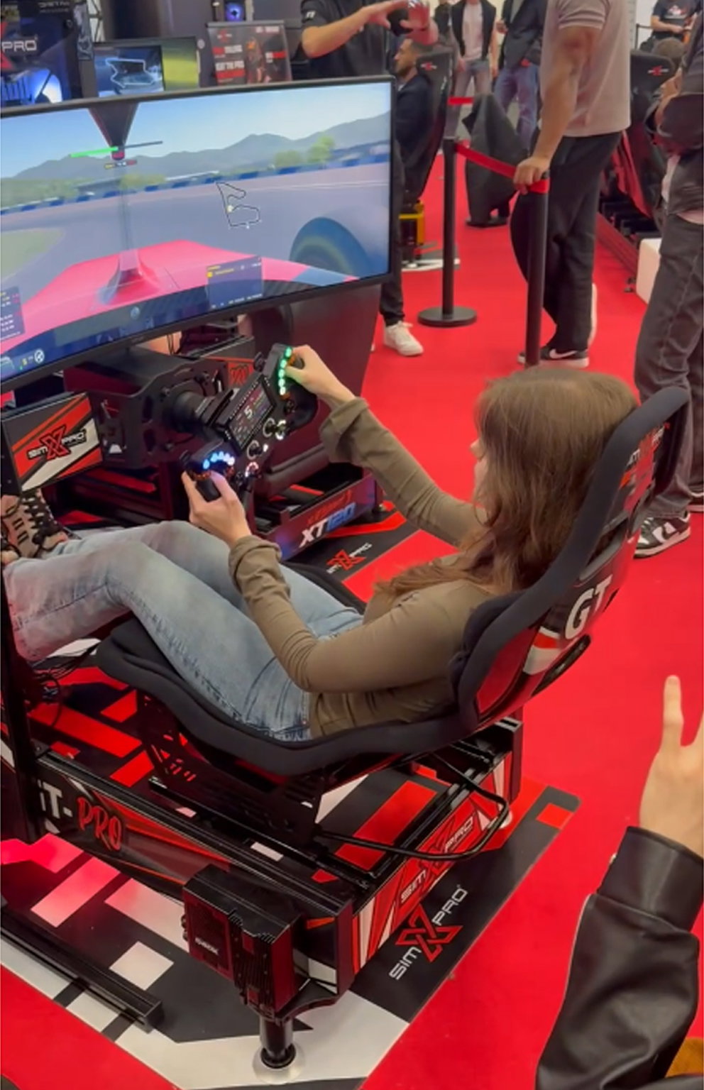 Visitor racing on a SimXPro rig with GT seat and curved screen on the red floor of the SimXPro booth
