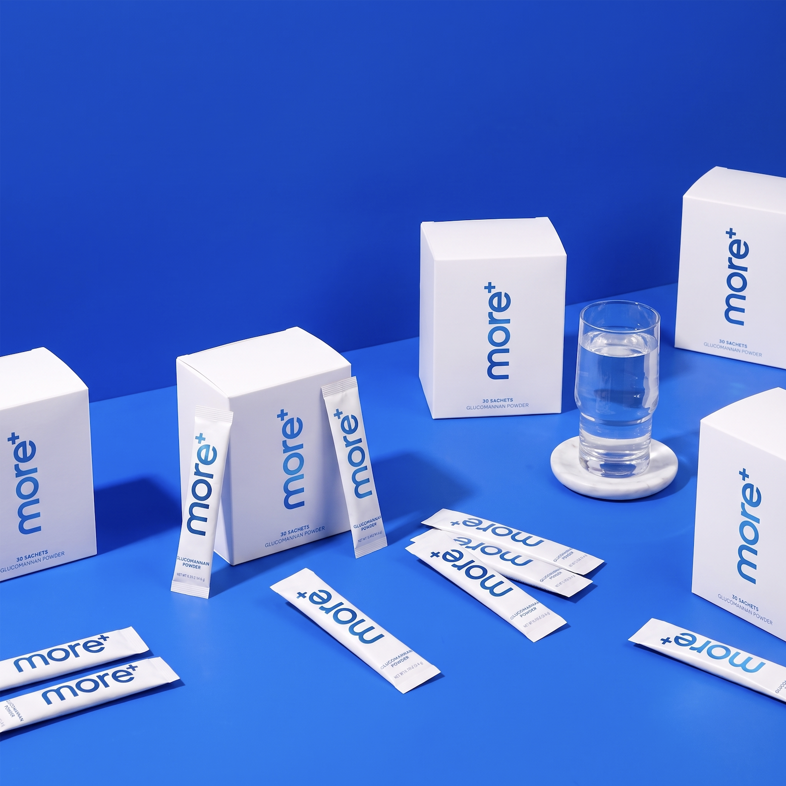 more+ glucomannan powder boxes and stick packs arranged with a glass of water on a bright blue background