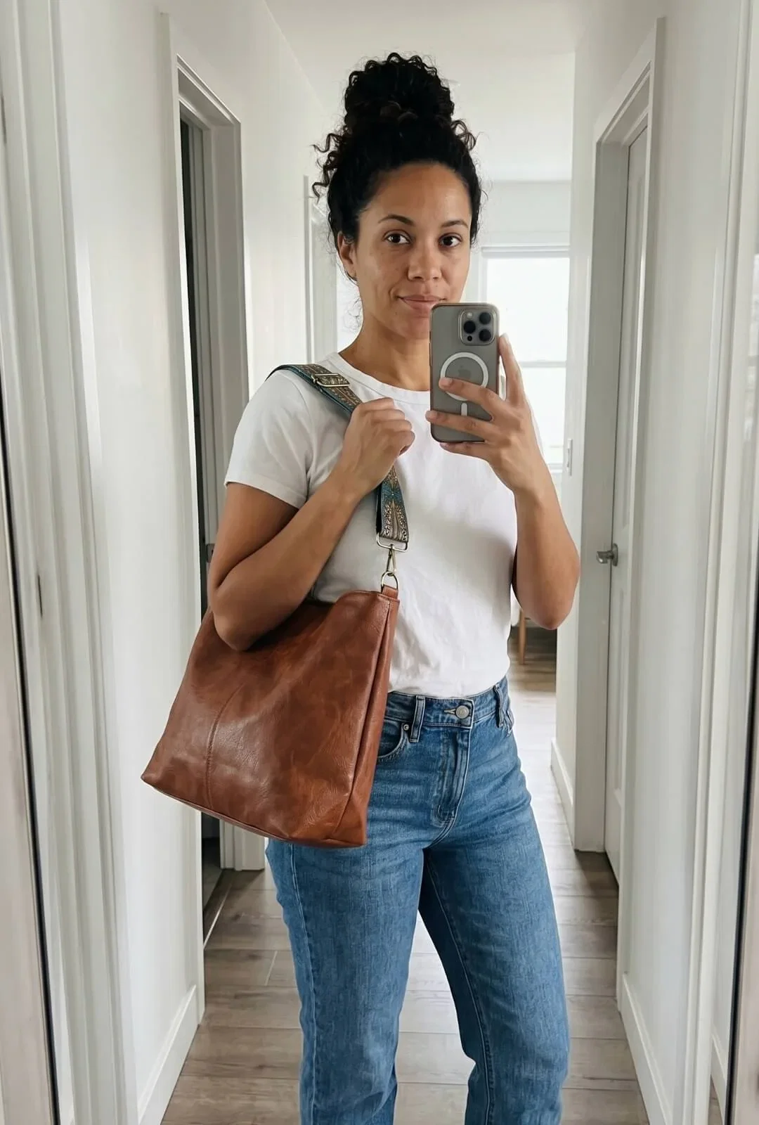 Customer photo: Mirror selfie in a white tee and jeans, wearing the bag on its patterned strap.