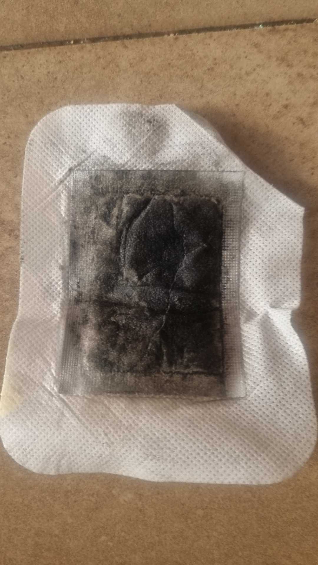 Customer photo of a single used SOONÉ foot patch laid on a tiled floor, its absorbent core turned almost black after being worn overnight.
