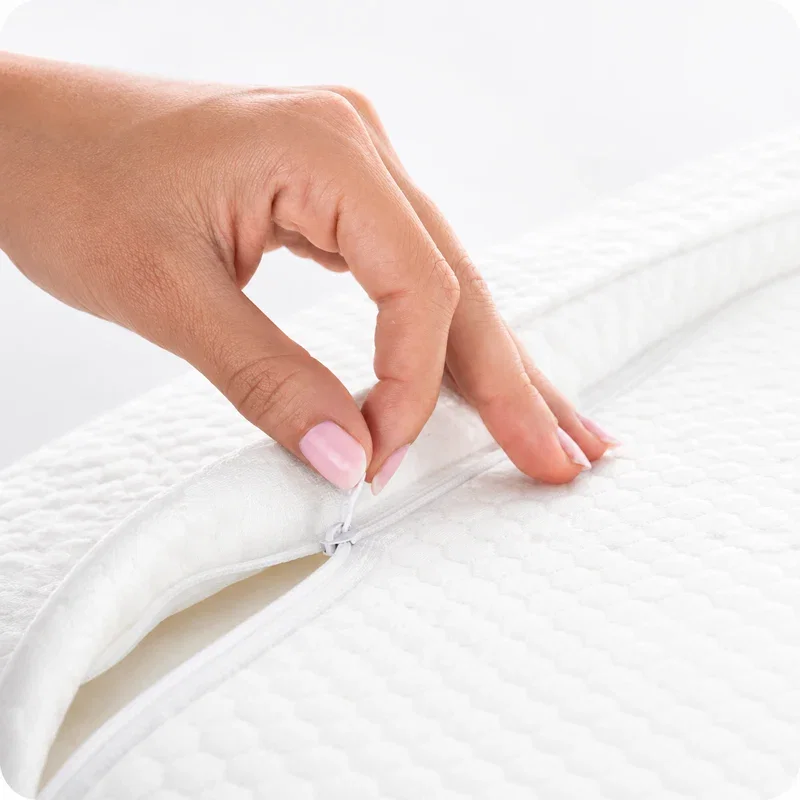 Hand pulling open the zipper along the edge of the white quilted pillow cover