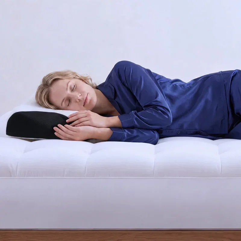 Woman in navy pyjamas sleeping on her side, hands resting by the contoured side of the black pillow