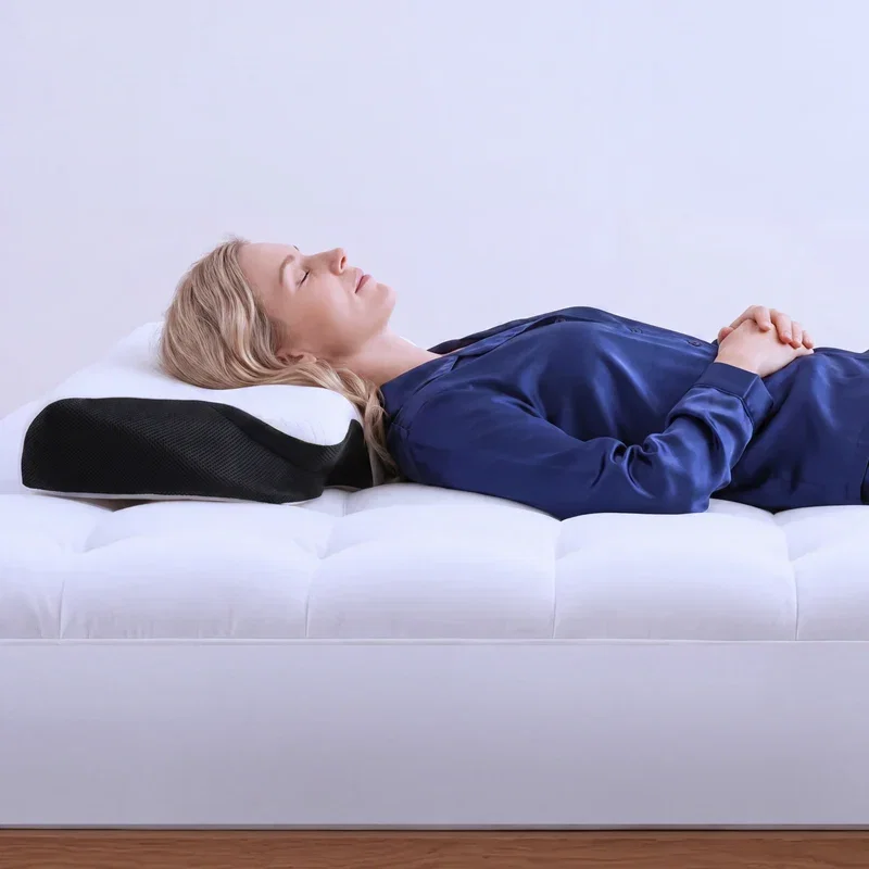 Woman in a navy shirt sleeping on her back, head resting in the soft center hollow of the black and white pillow