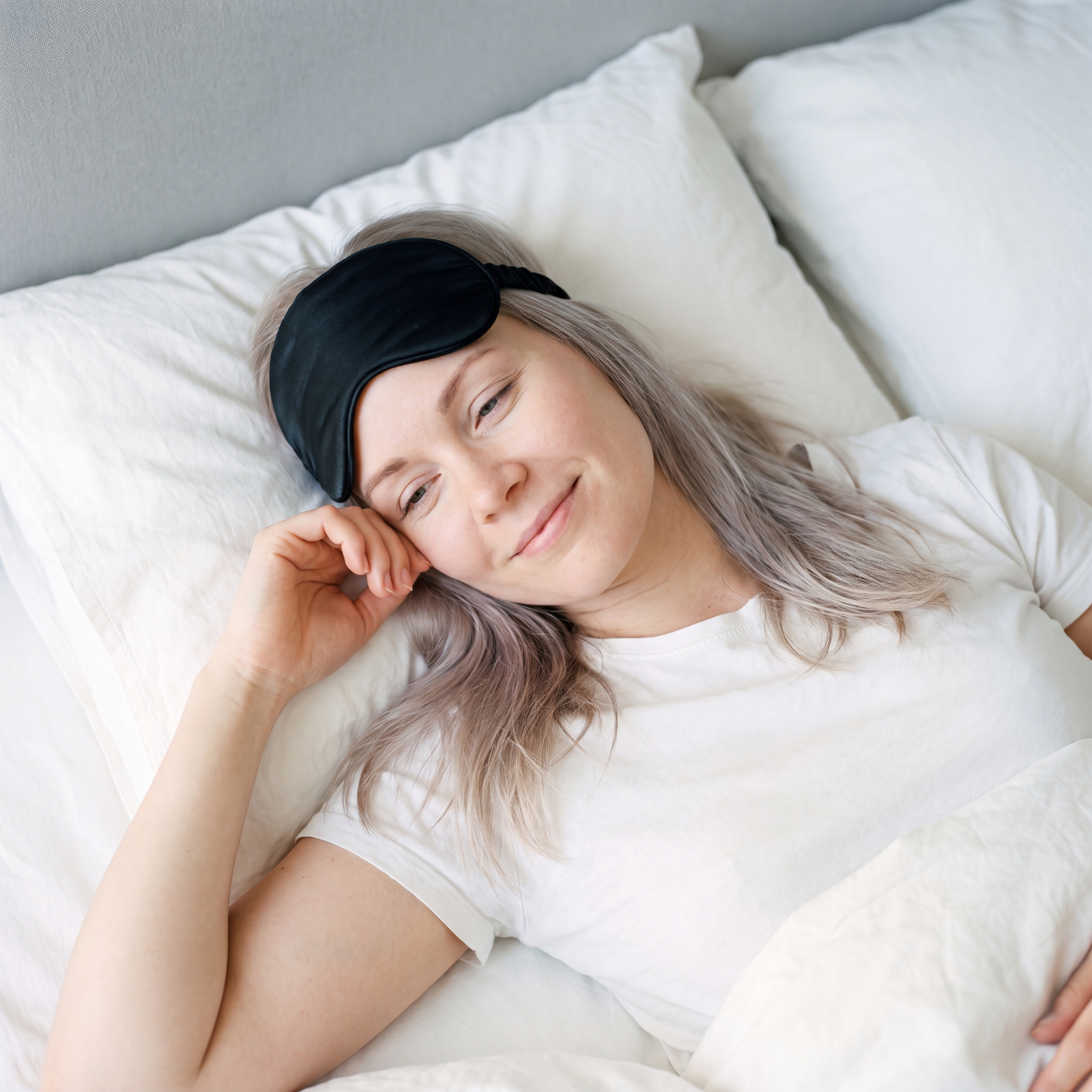 Smiling woman resting in bed with a sleep mask pushed up on her forehead