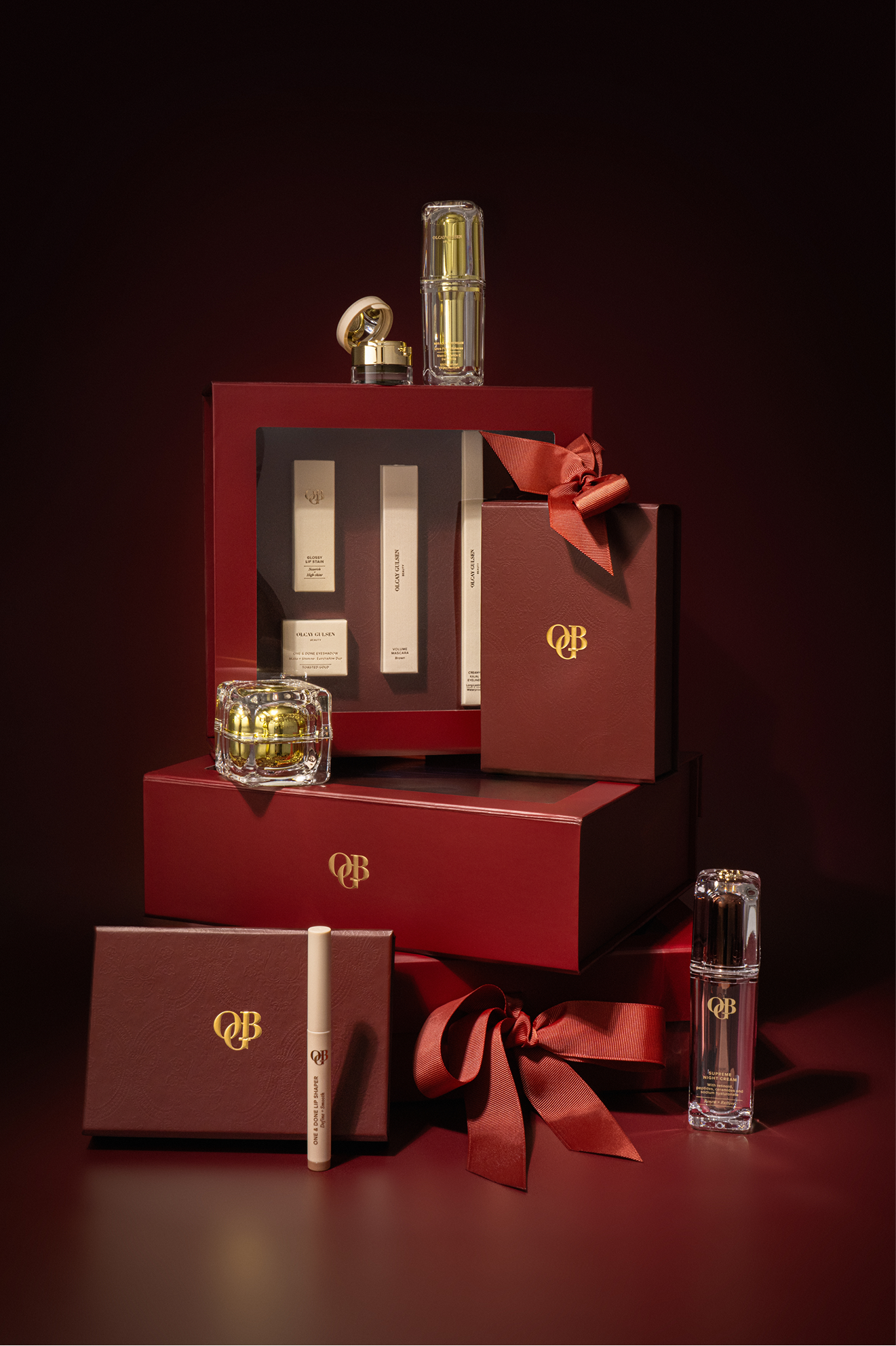 An OGB skincare gift set in an open crimson box surrounded by stacked red gift boxes with bronze bows
