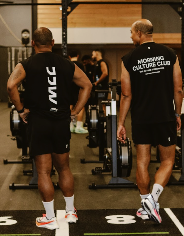 Two members of the Morning Culture Club between rowing machines in black MCC training kit