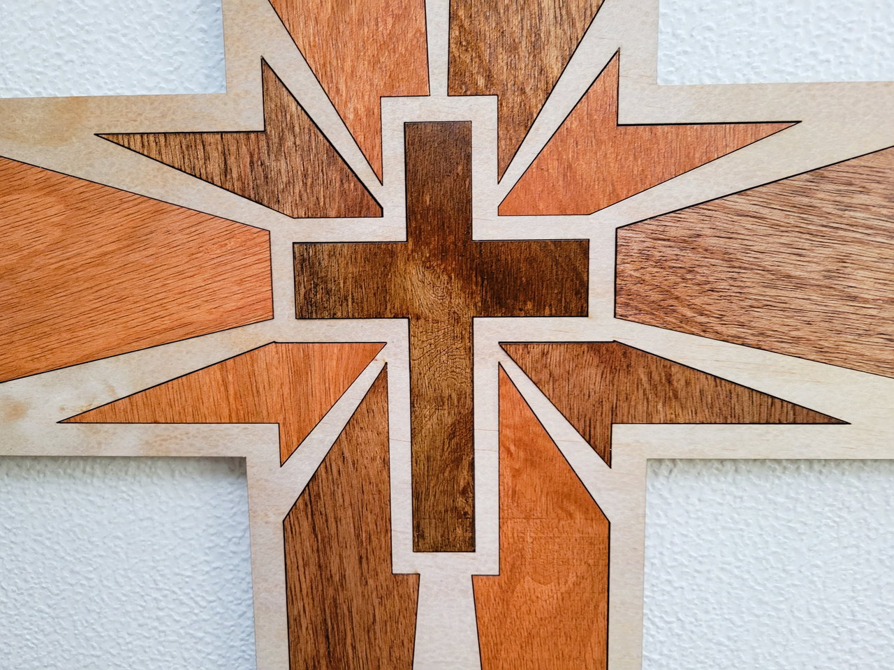 Decorative wooden cross with geometric starburst pattern on textured white wall