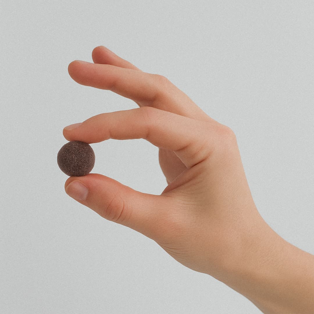 A hand holding a small, brown anti-stress gummy, against a plain light background.