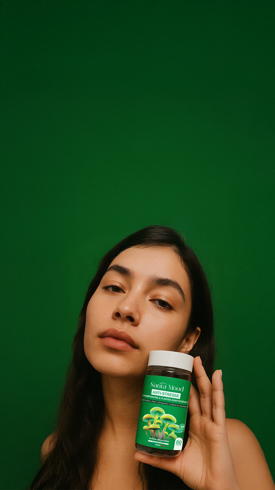 Person holding a bottle of Santa Mood Anti-Stress supplements against a green background.
