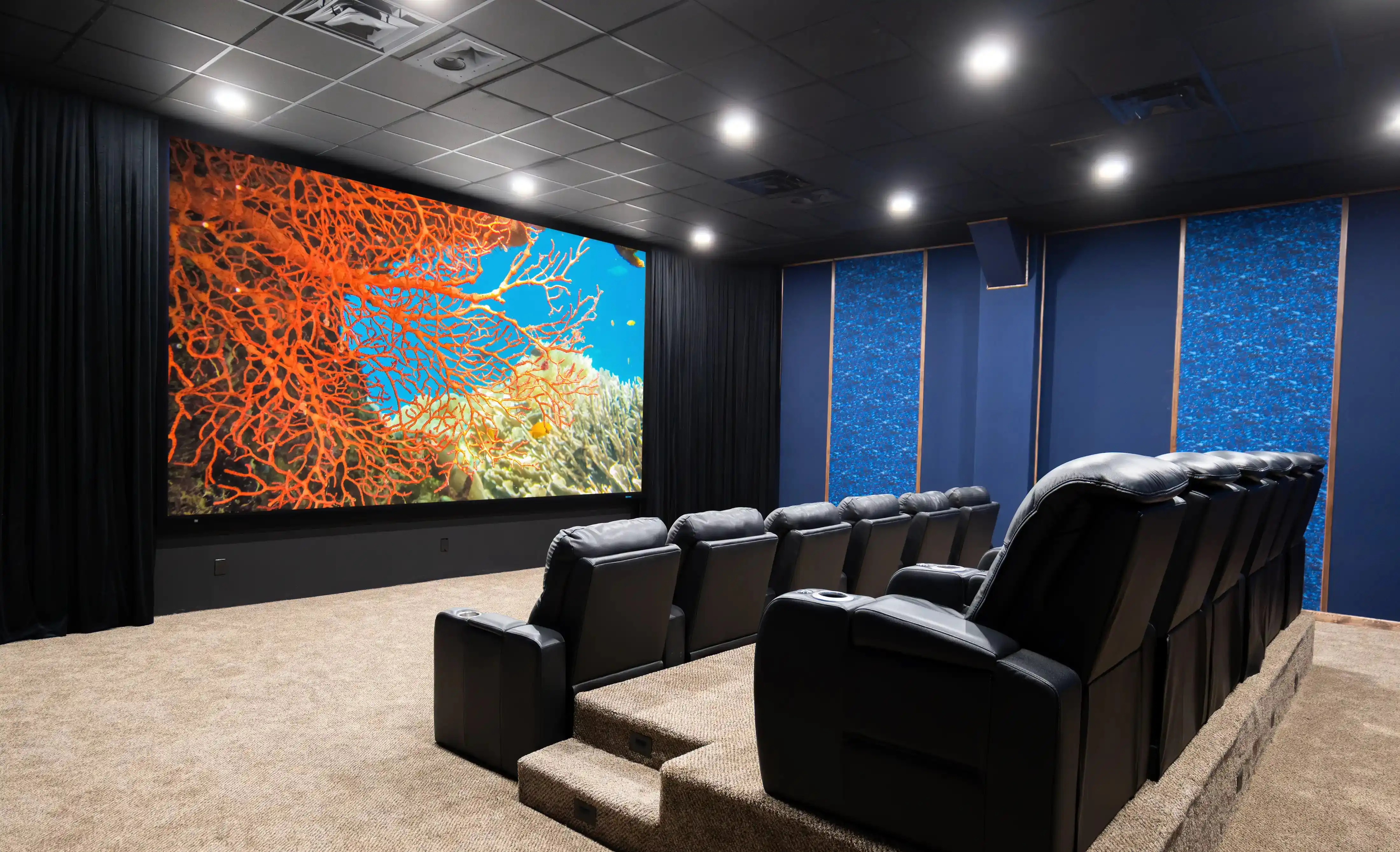 Dedicated home theater with a large screen showing a coral reef and tiered black leather recliners
