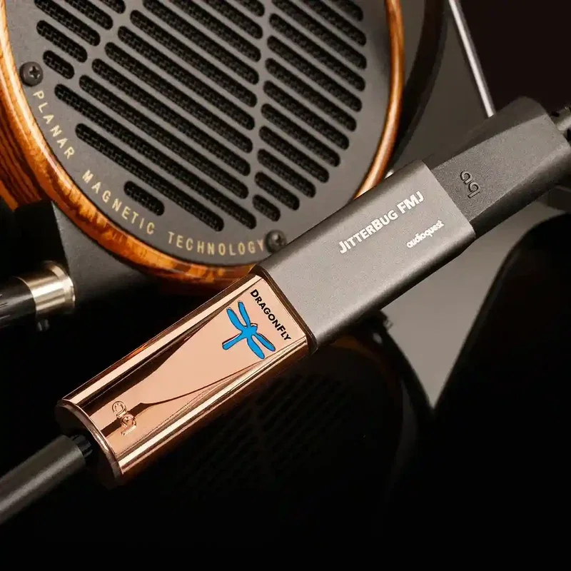Copper AudioQuest DragonFly USB DAC plugged into a JitterBug FMJ, in front of a wood-ringed planar magnetic headphone