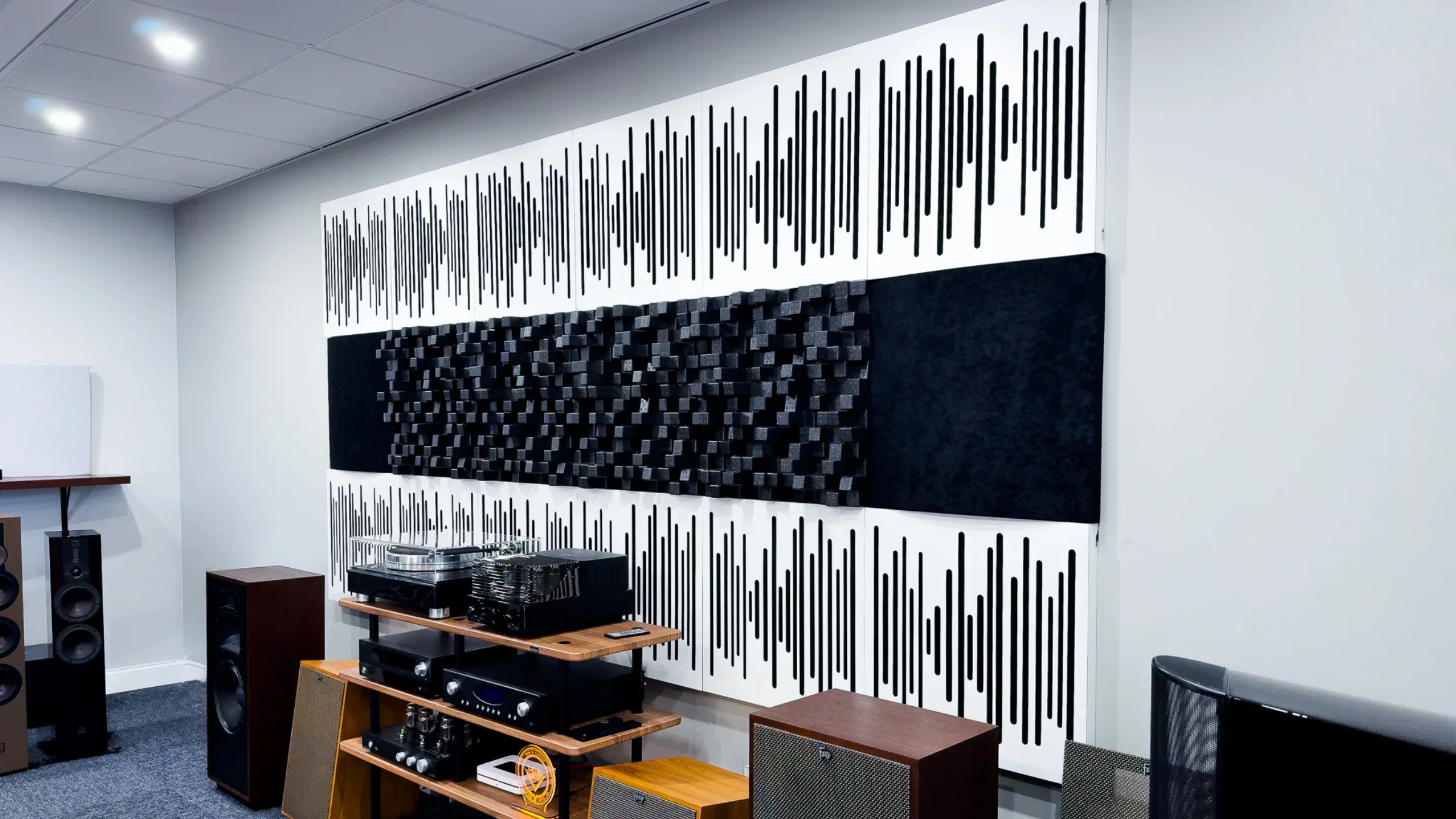 Audiolab listening room with a full wall of white slat acoustic panels and black diffuser blocks behind a rack of hi-fi components, a turntable and floorstanding speakers