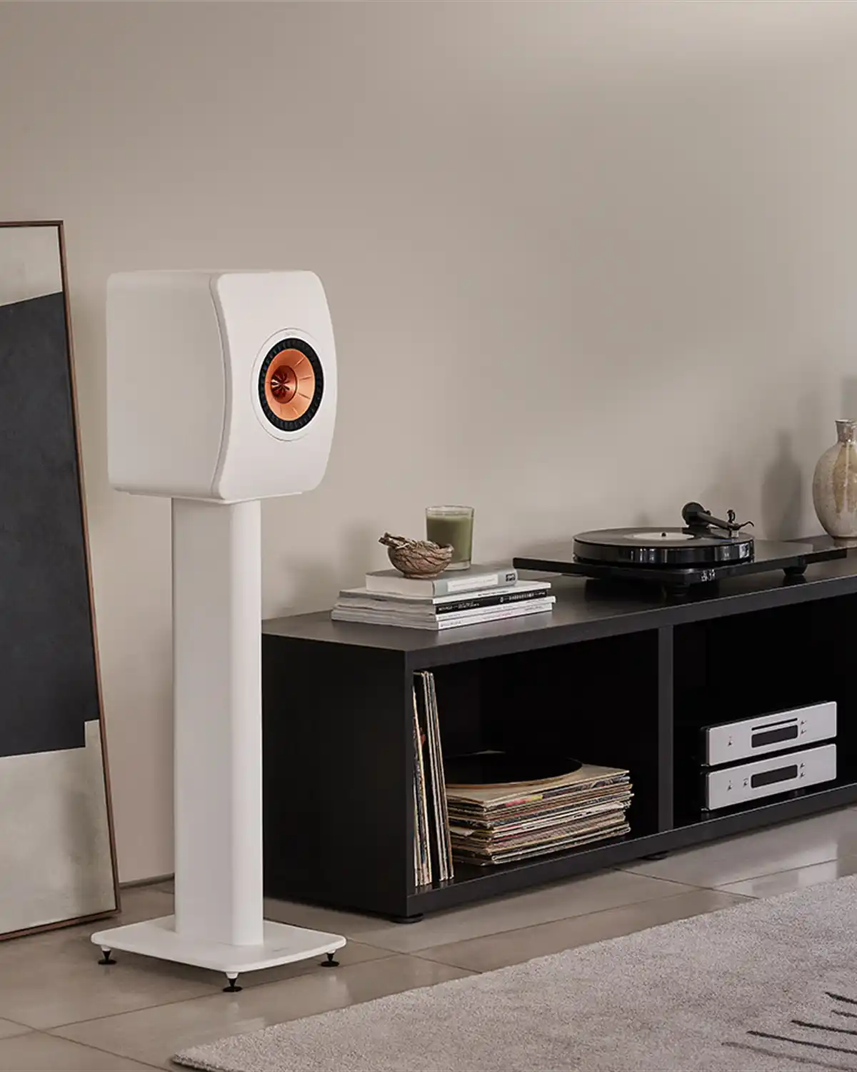 White KEF LS50 speaker with a copper Uni-Q driver on a stand, beside a turntable and a vinyl collection