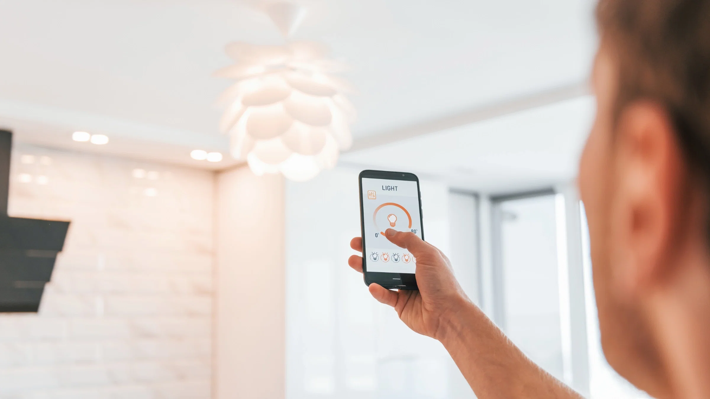Homeowner adjusting a smart lighting scene from a phone app beneath a modern pendant light