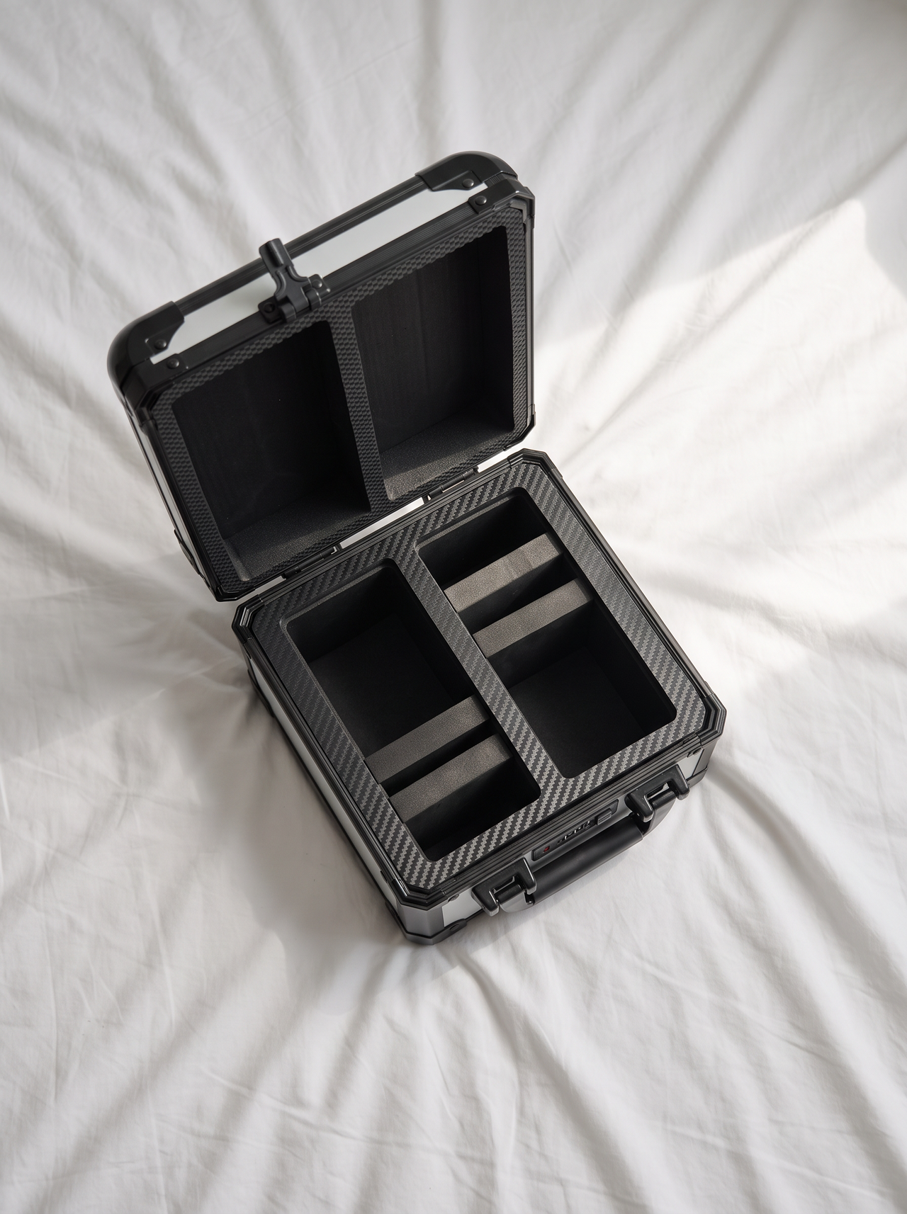 Black storage case with compartments open on white crumpled bed sheets