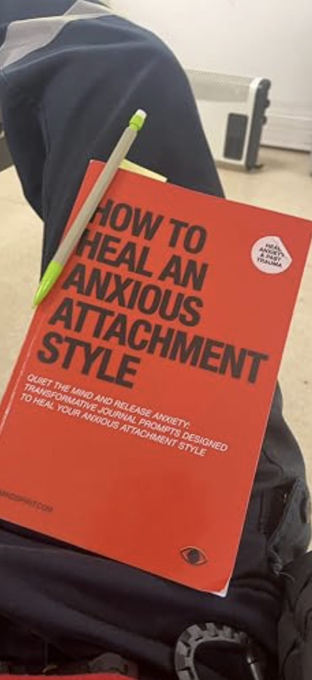 Customer photo of the orange How to Heal an Anxious Attachment Style journal resting on a lap with a pen on the cover.