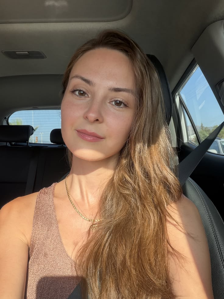 Customer photo of Elora R. smiling softly at the camera in her car in warm afternoon sunlight.