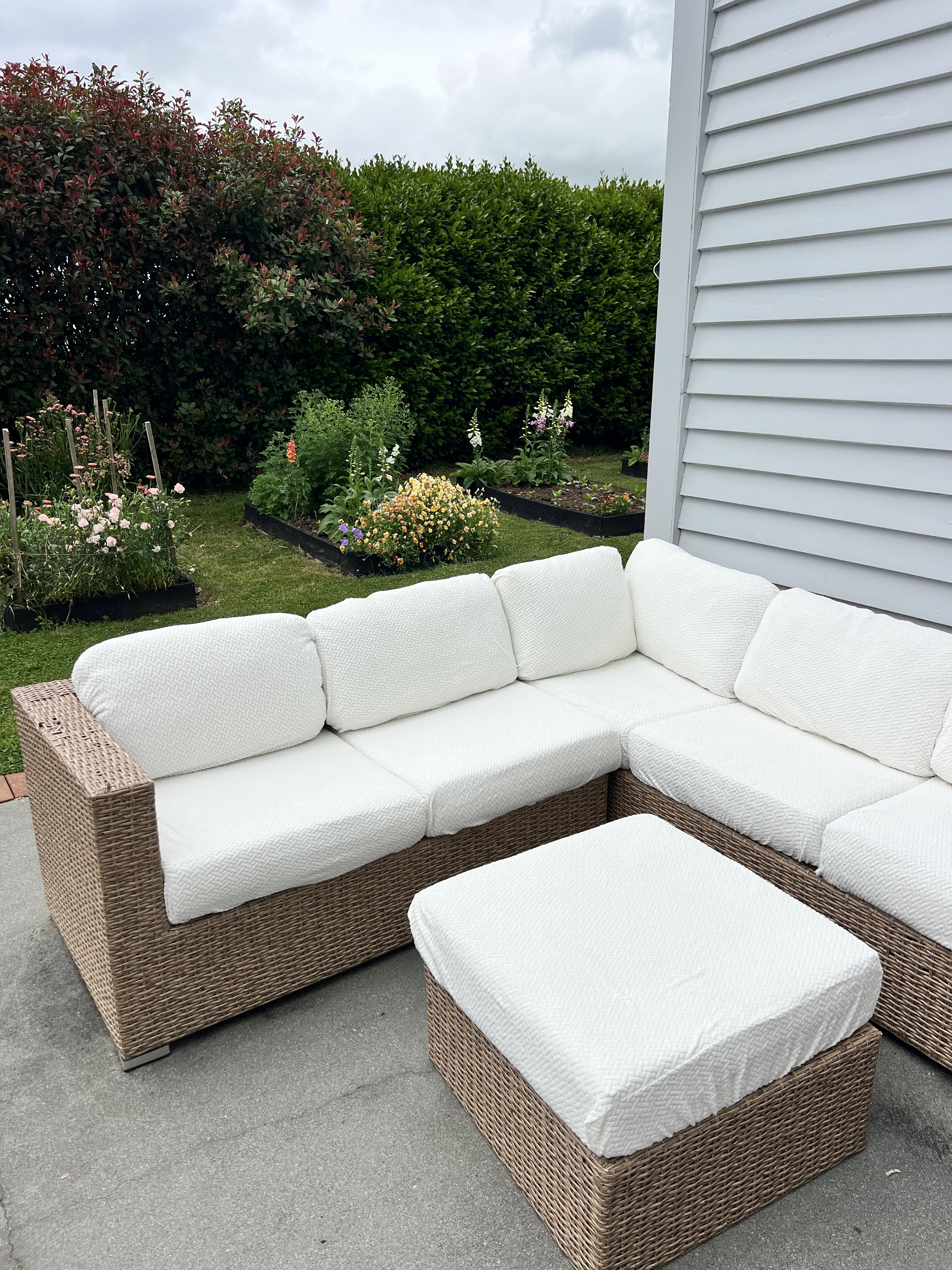 After: the wicker corner lounge and ottoman with clean white textured covers in front of the garden beds