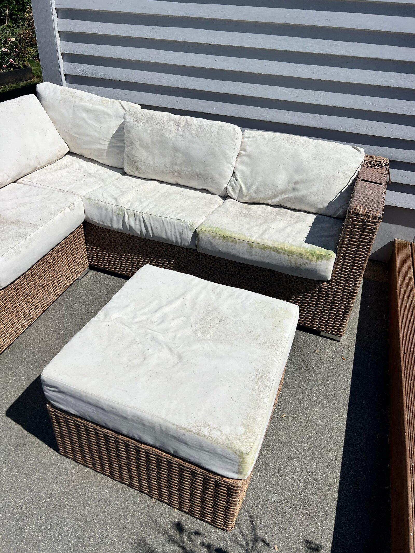White wicker outdoor lounge with mouldy, stained cushions on a suburban patio