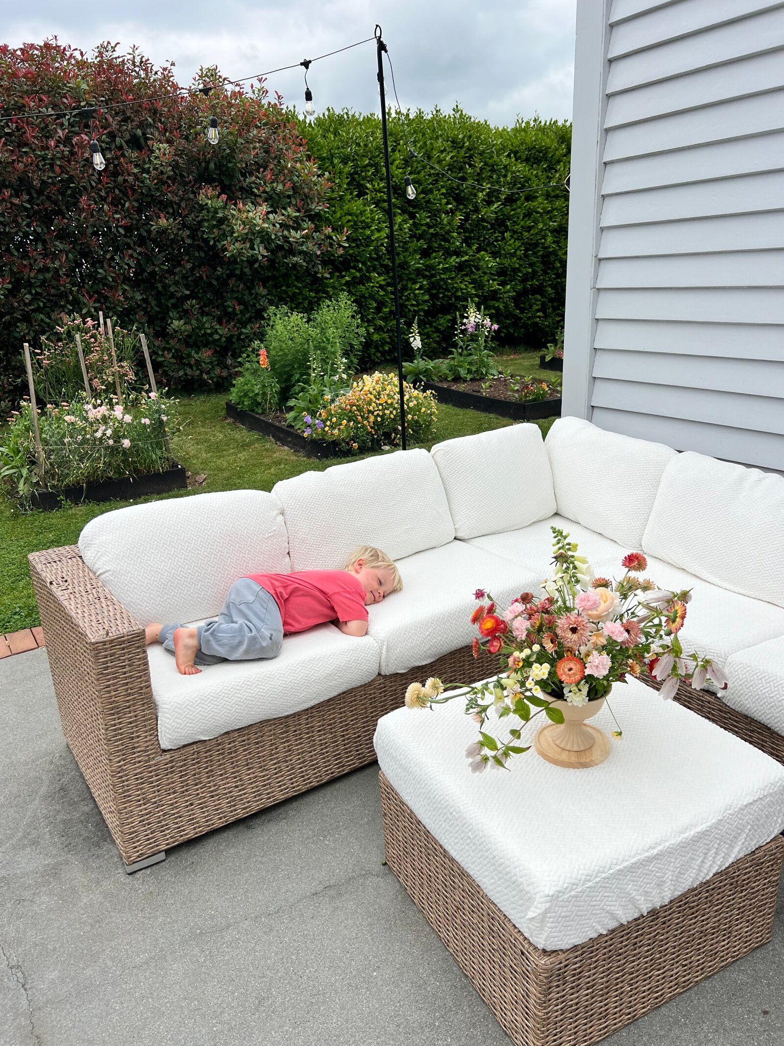 A young boy asleep on the restored outdoor couch with fresh flowers on the ottoman