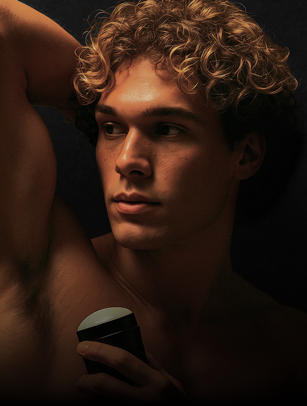 A young man with curly hair holding a deodorant stick