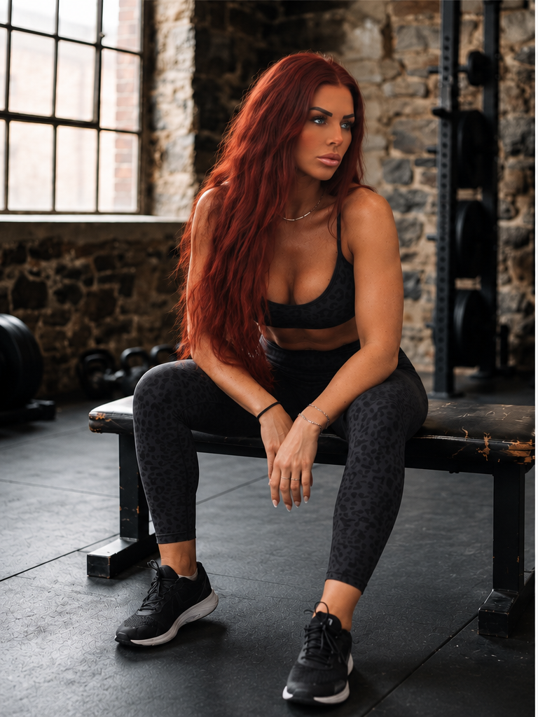 Charlotte Svenningsen med langt rødt hår i sort træningstøj, siddende på en træningsbænk i et fitnesscenter