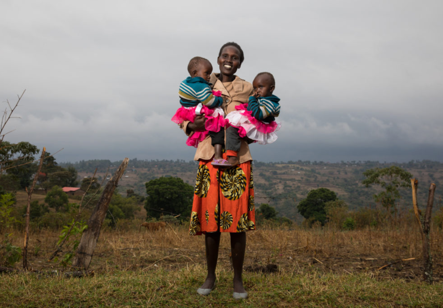 Smiling mother standing in a rural landscape, holding her two young children in pink tutus