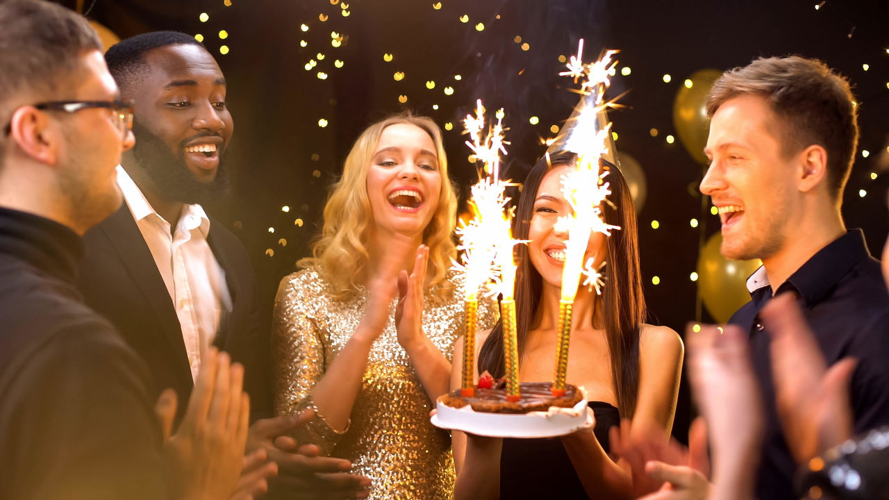Friends celebrating a birthday with gold cake sparklers on a chocolate cake at an elegant party