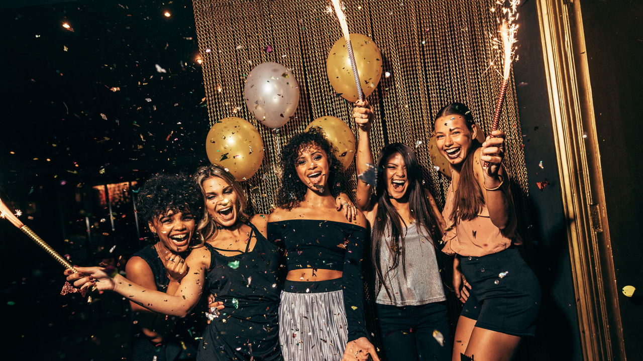 Group of friends holding gold party sparklers with balloons and confetti at a New Year's Eve celebration