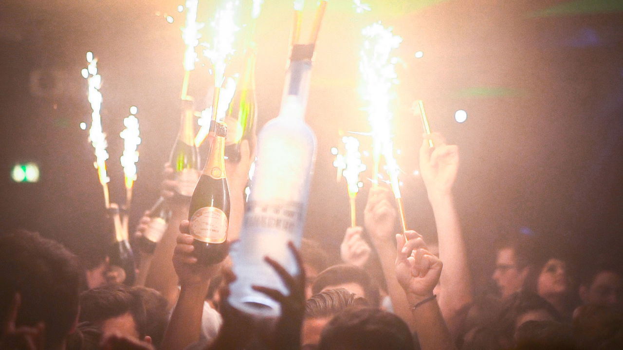 Champagne and vodka bottles held up with lit bottle sparklers in a crowded nightclub
