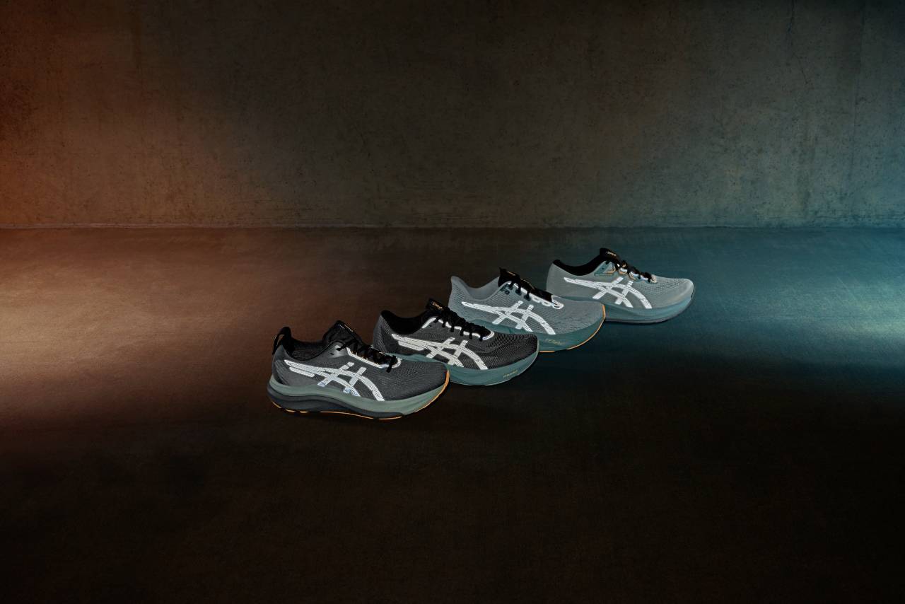 Four ASICS Lite-Show running shoes with reflective stripes lined up on a dark studio floor