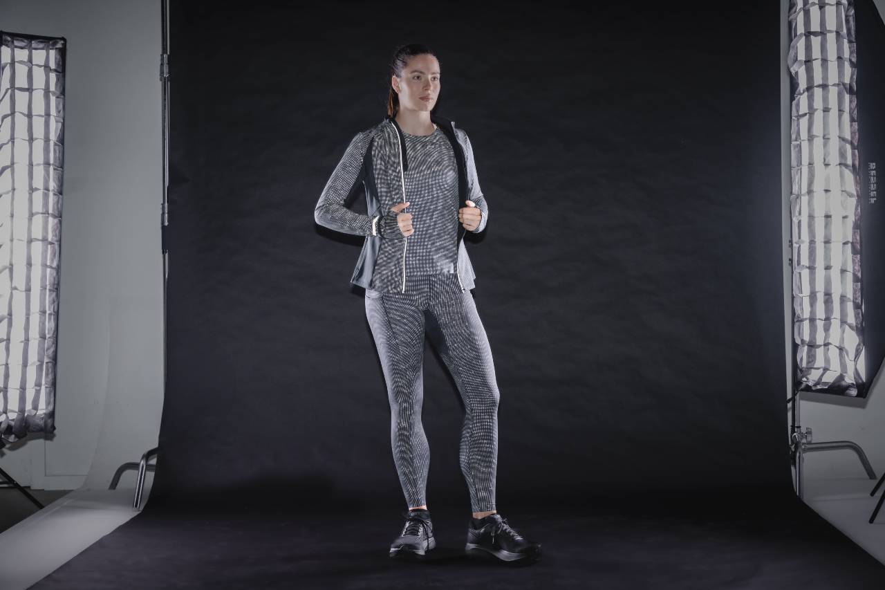 Woman in a reflective running jacket, top and leggings standing in a dark studio