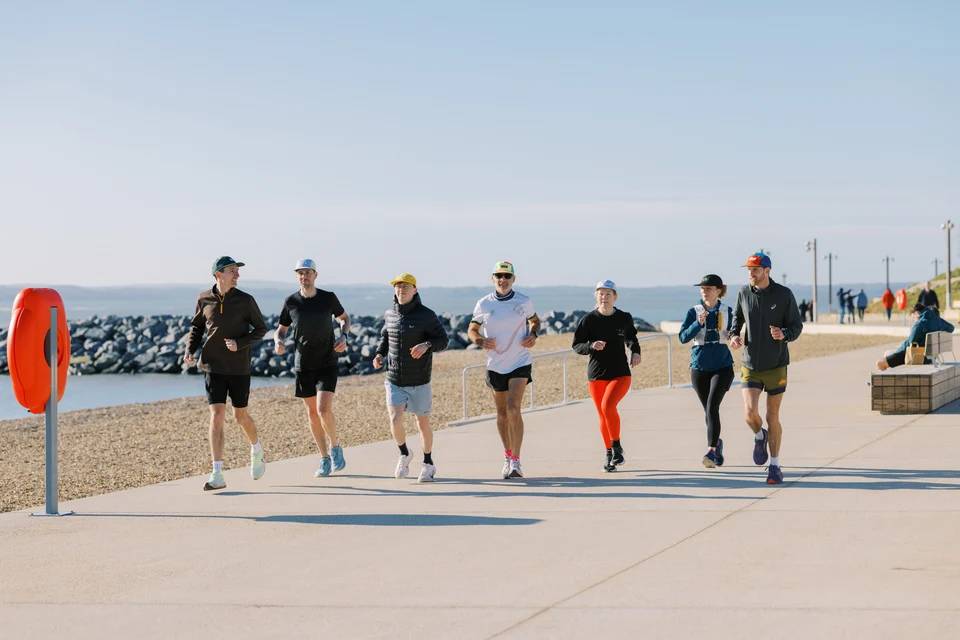 A group of runners wearing colourful Runr caps running together along a sunny seafront promenade