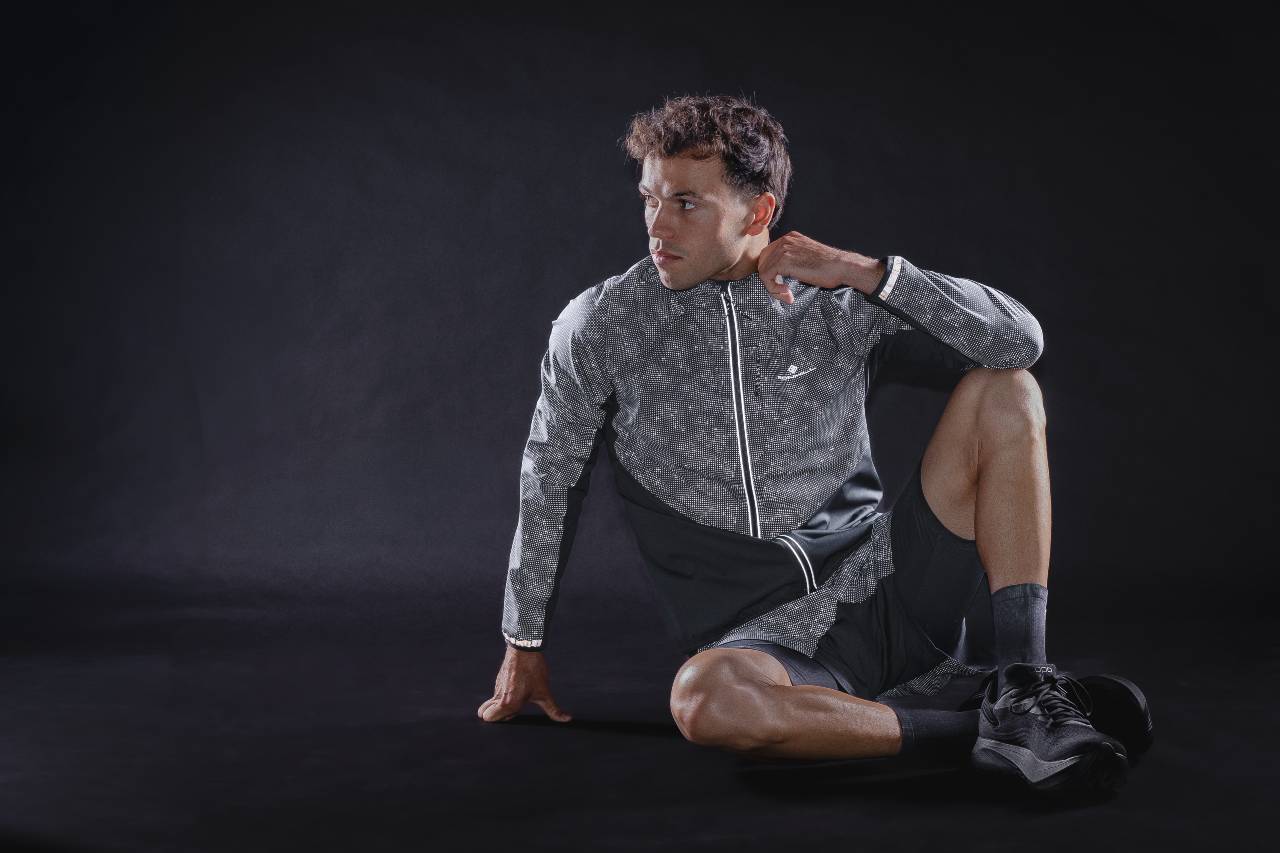 Runner seated in the Ronhill AW26 reflective jacket against a black studio backdrop