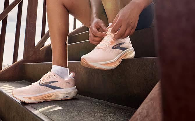 A runner sitting on outdoor steps lacing up a pair of peach Brooks Ghost trainers