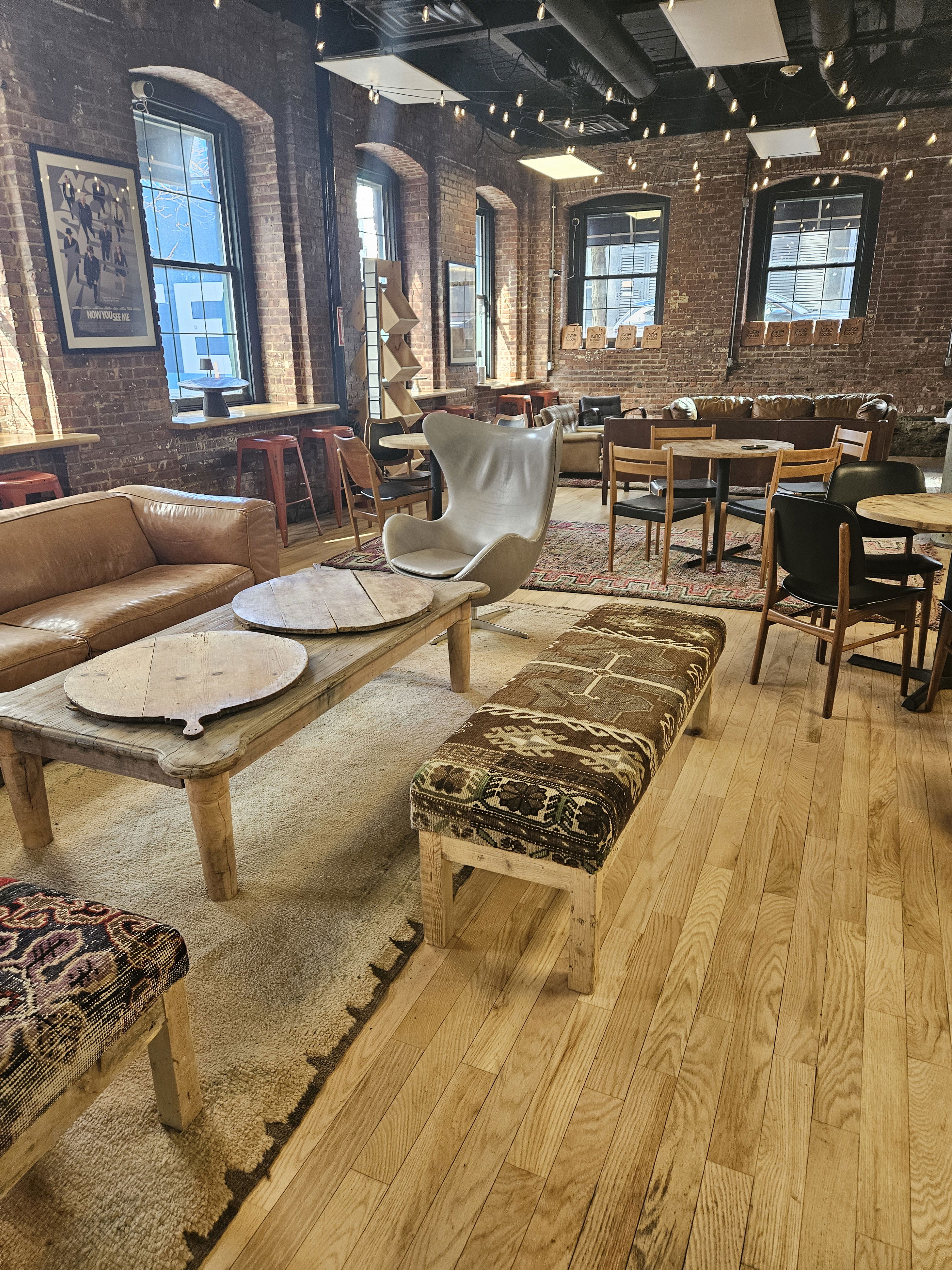 A cozy cafe with brick walls, various seating, wooden tables, and warm lighting.