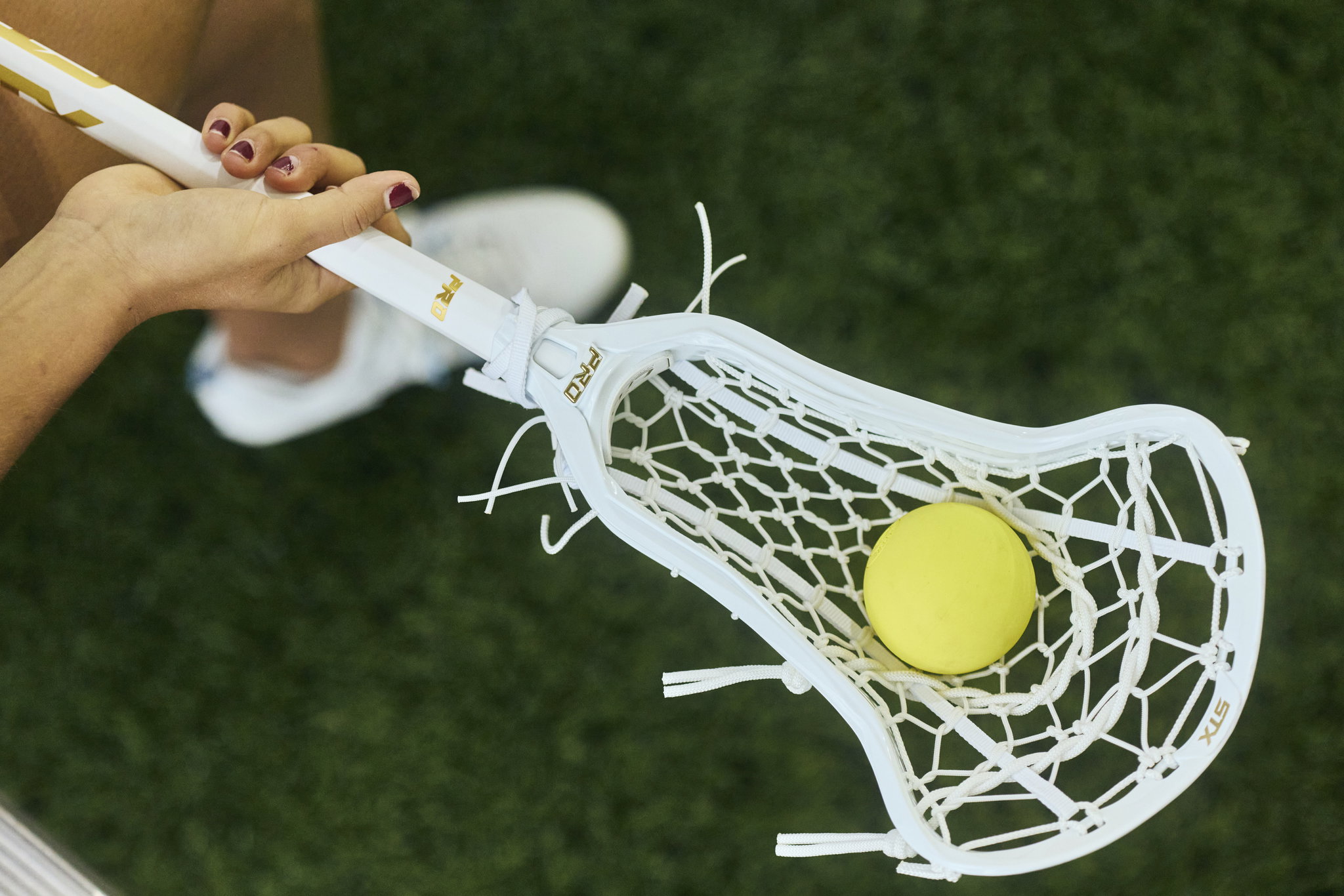 Overhead view of Chloe's hands on the shaft of her white Crux Pro, a yellow ball sitting in the pocket on turf